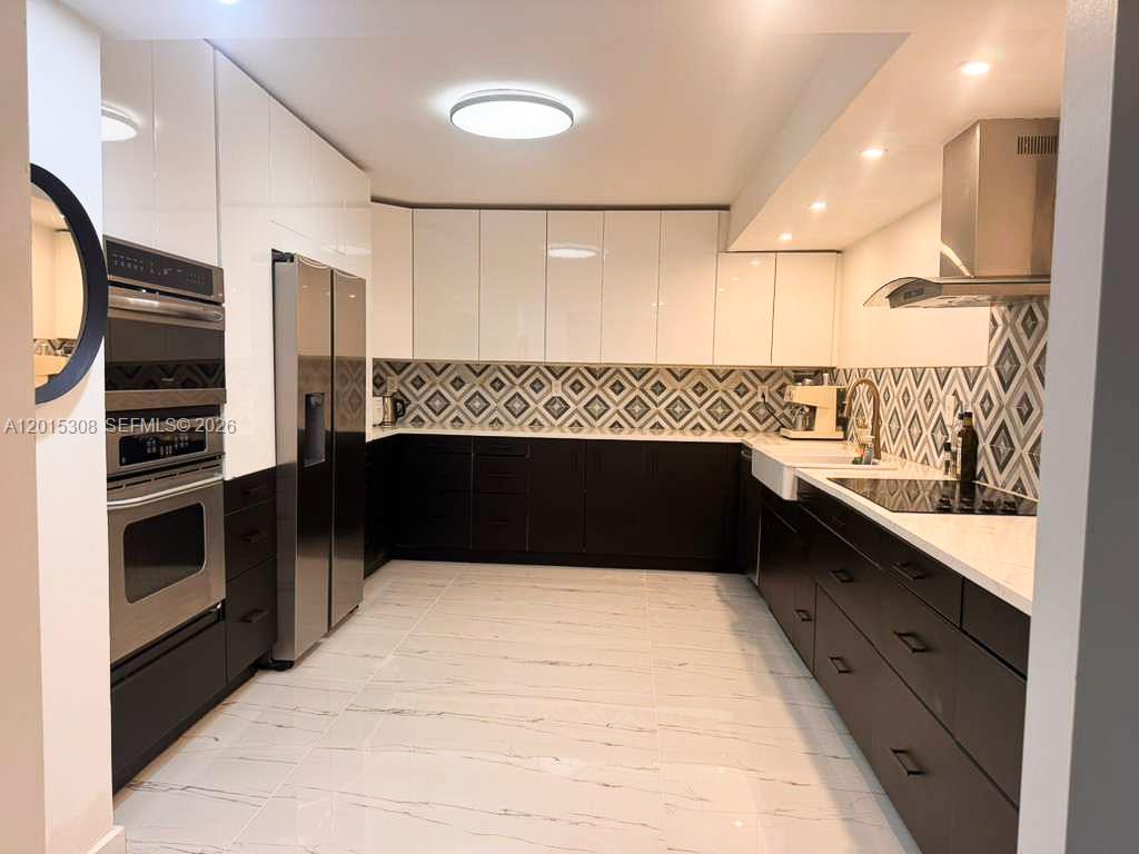 A modern kitchen features white upper cabinets, dark lower cabinets, and a patterned tile backsplash — 500 Three Islands Blvd # 106, Hallandale Beach FL 33009, HALLANDALE BEACH, FL