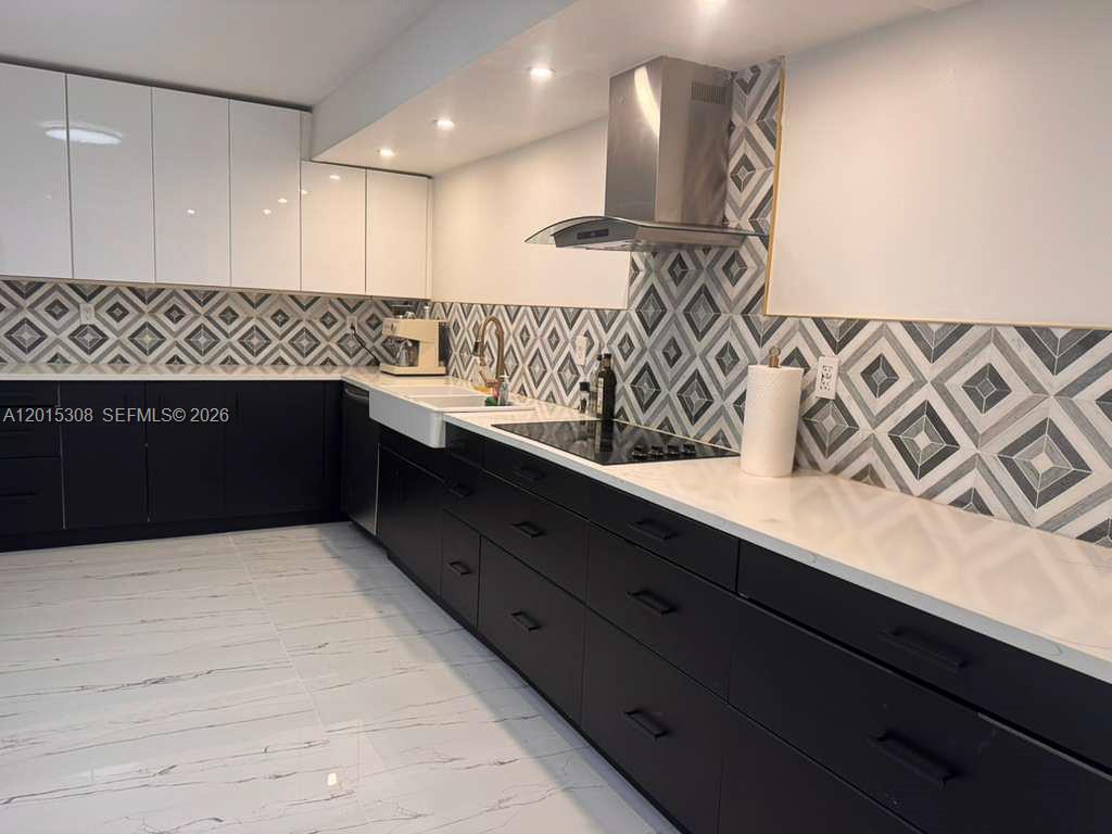 A modern kitchen features black lower cabinets, white upper cabinets, and a geometric patterned backsplash — 500 Three Islands Blvd # 106, Hallandale Beach FL 33009, HALLANDALE BEACH, FL