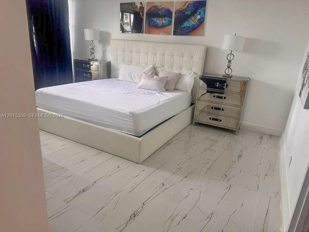 A bedroom features a tufted white bed, mirrored nightstands, and white marble-patterned tile flooring — 500 Three Islands Blvd # 106, Hallandale Beach FL 33009, HALLANDALE BEACH, FL