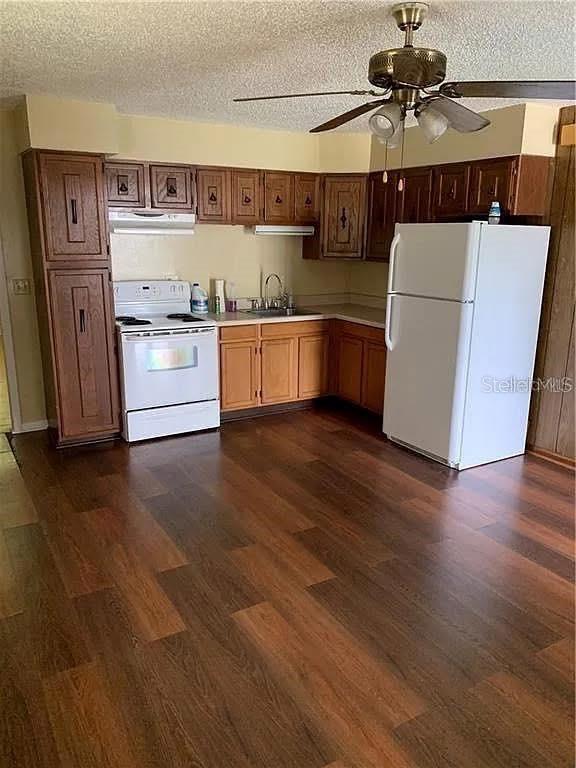 A kitchen features wood cabinets, a white stove, a white refrigerator, and dark wood flooring — 5217 17TH STREET, ZEPHYRHILLS, FL