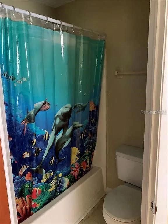 A bathroom features a white toilet next to a shower with an ocean-themed curtain — 5217 17TH STREET, ZEPHYRHILLS, FL