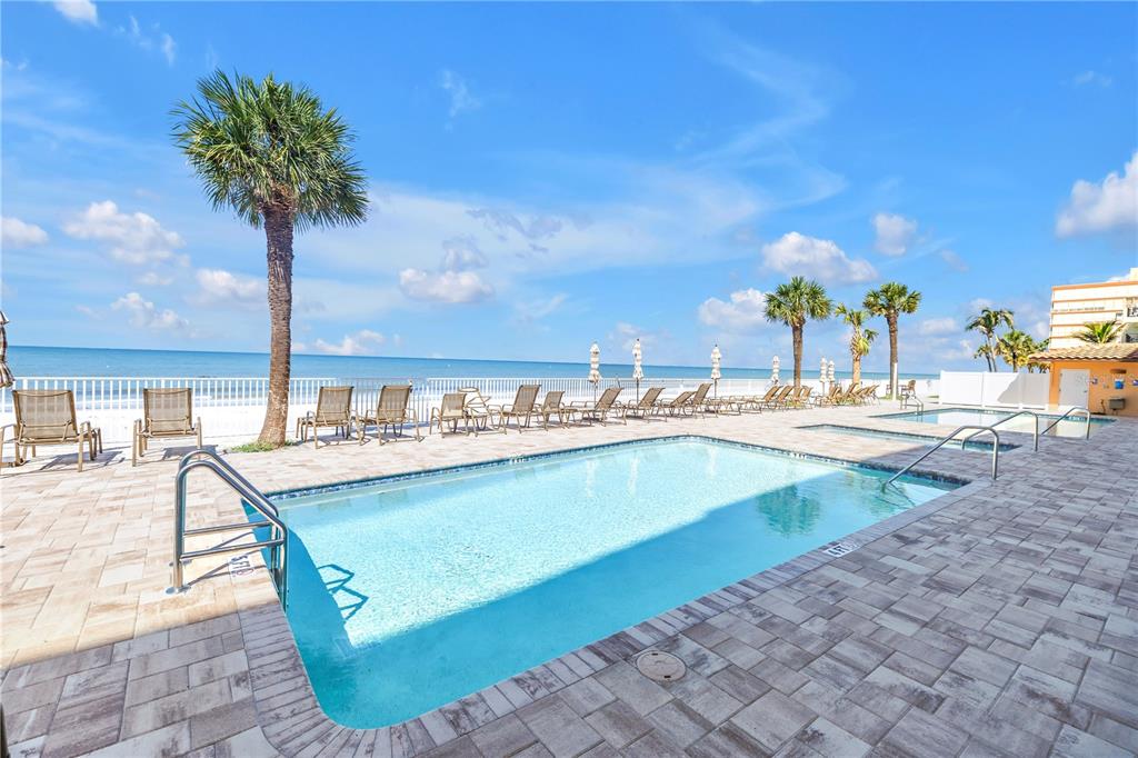A swimming pool with lounge chairs sits on a patio overlooking the ocean and beach — 16326 GULF BOULEVARD UNIT 308, REDINGTON BEACH, FL