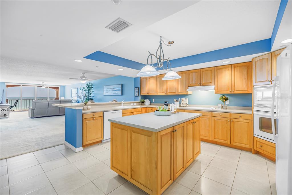 A kitchen with light wood cabinets, a central island, and blue walls opens to a living area — 16326 GULF BOULEVARD UNIT 308, REDINGTON BEACH, FL