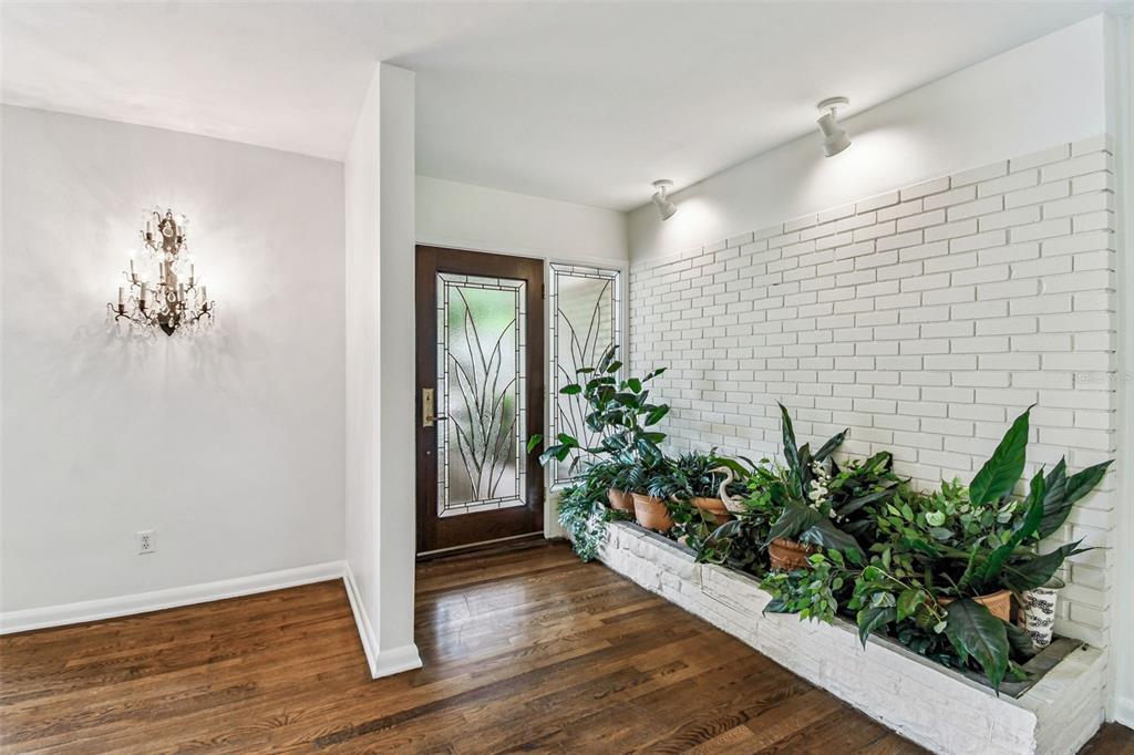 An entryway features hardwood floors, a white brick planter with plants, and a decorative chandelier — 4508 HENDERSON BOULEVARD, TAMPA, FL