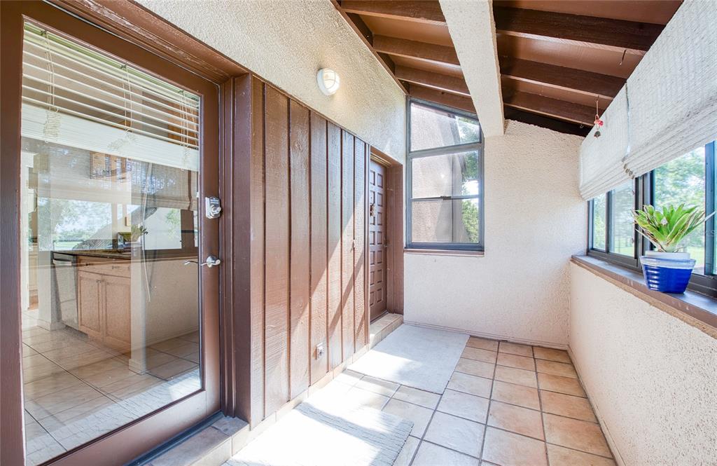 A sunroom features tiled flooring, wood-paneled walls, a glass door, and large windows — 6305 PELICAN CREEK CROSSING UNIT D, ST PETERSBURG, FL