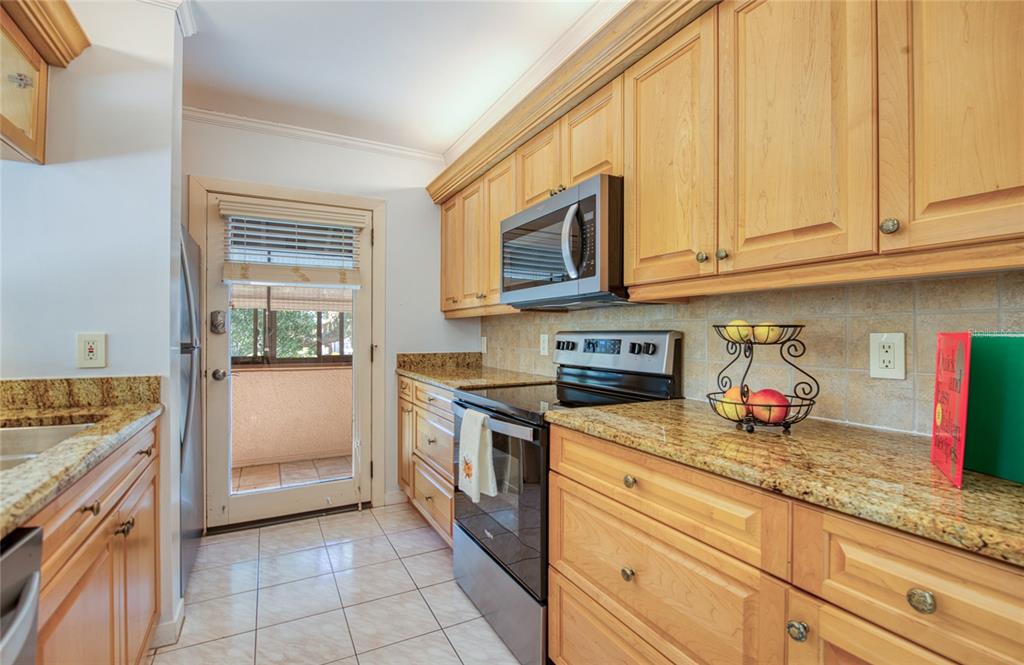 A kitchen with light wood cabinets, granite countertops, stainless steel appliances, and a glass door — 6305 PELICAN CREEK CROSSING UNIT D, ST PETERSBURG, FL