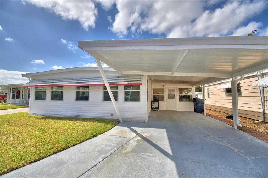 A white mobile home with a carport and a concrete driveway under a blue sky — 145 HOLIDAY LANE, AUBURNDALE, FL
