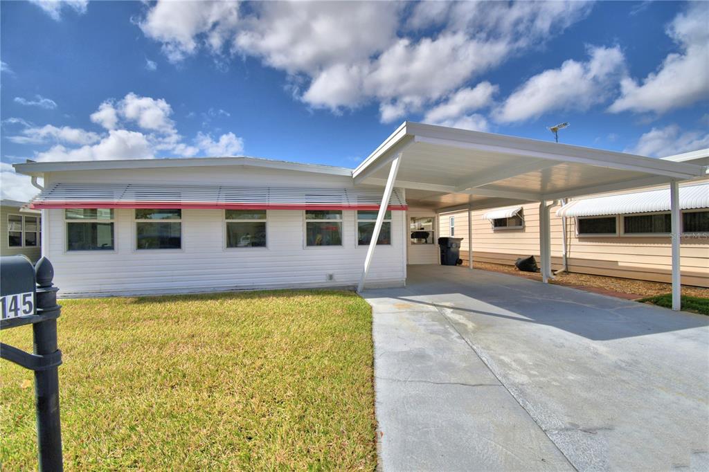 A white single-story manufactured home features a carport and a front lawn — 145 HOLIDAY LANE, AUBURNDALE, FL