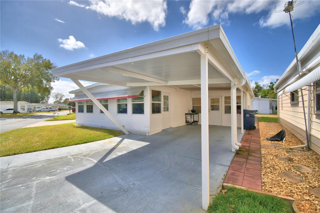A white mobile home features a concrete carport and a paved walkway along the side — 145 HOLIDAY LANE, AUBURNDALE, FL