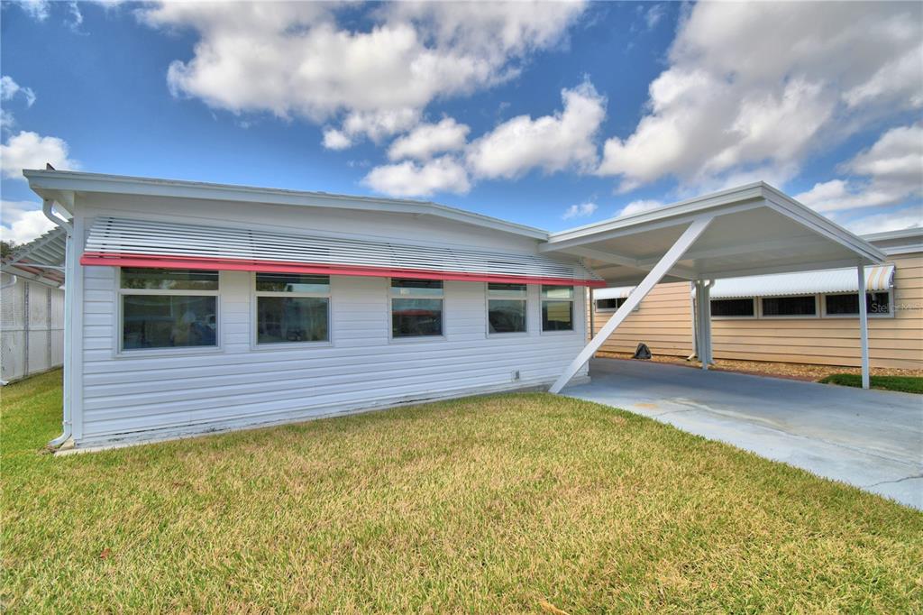 A white mobile home exterior features a metal awning over windows and an attached carport — 145 HOLIDAY LANE, AUBURNDALE, FL