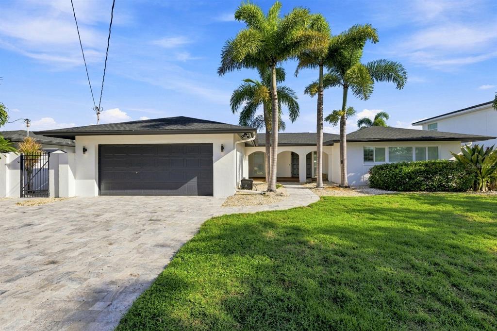 A white single-story house with a dark garage door, palm trees, and a paved driveway — 320 PALM ISLAND NE, CLEARWATER BEACH, FL