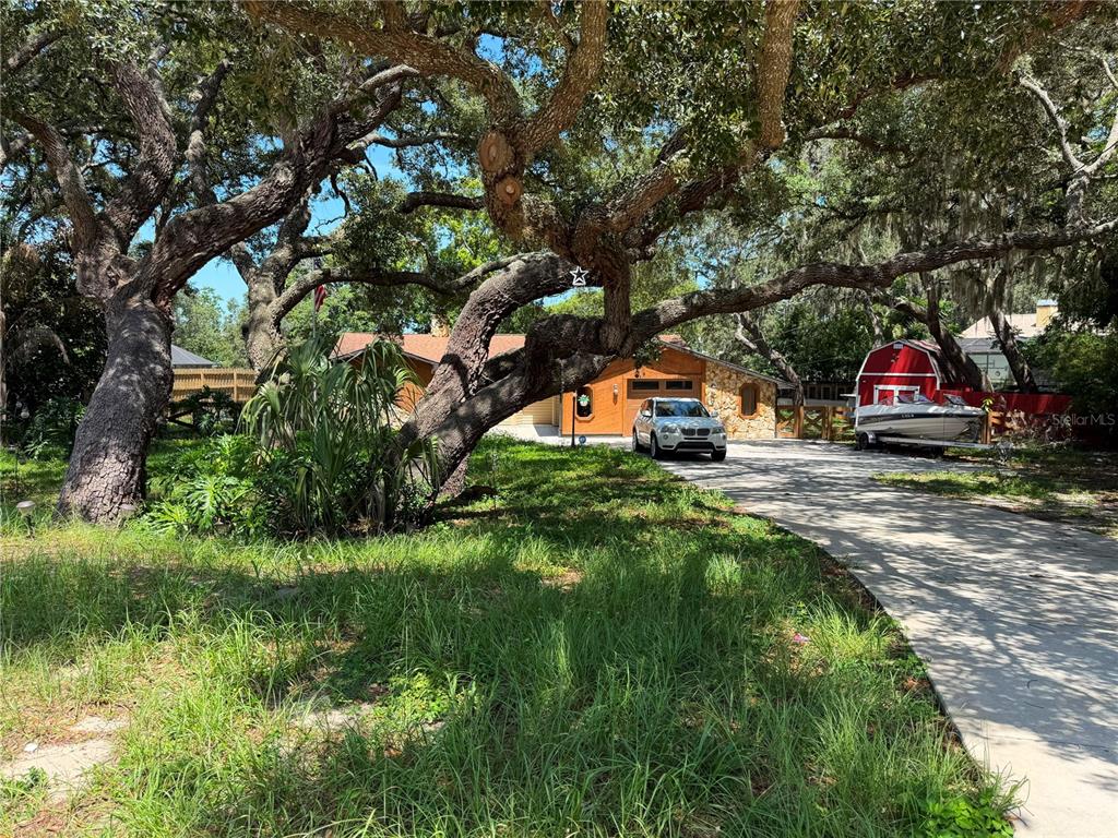 A white SUV is parked in the driveway of a house shaded by large oak trees — 325 GULFPORT LANE, SPRING HILL, FL