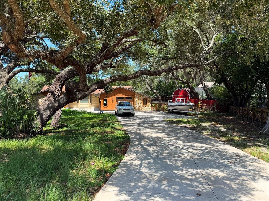 A single-story house with a stone facade and a long driveway featuring a parked boat — 325 GULFPORT LANE, SPRING HILL, FL