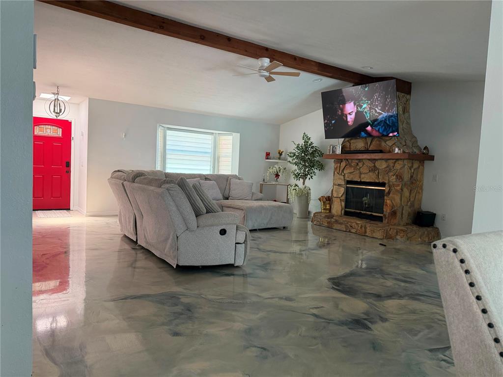 A living room features a stone fireplace, a gray sectional sofa, and marbled epoxy flooring — 325 GULFPORT LANE, SPRING HILL, FL