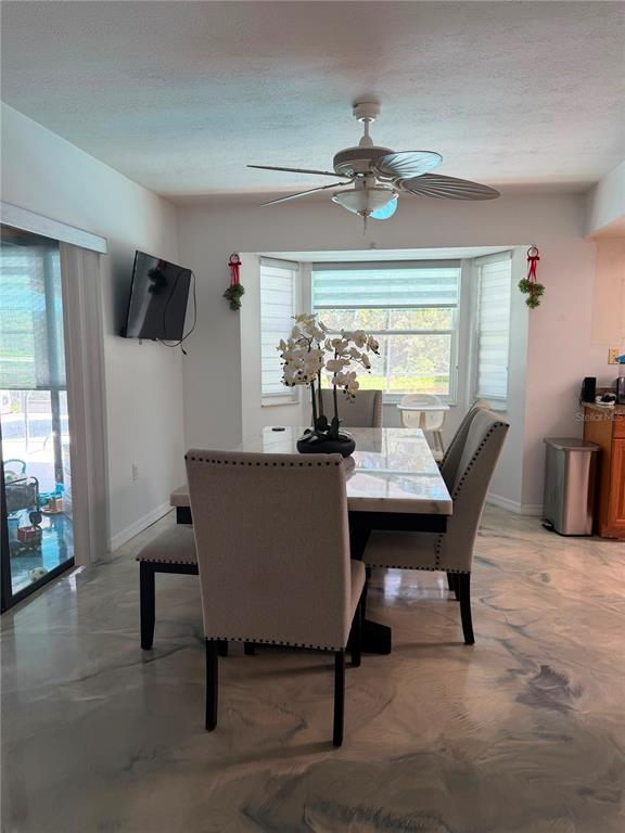 A dining area features a marble-topped table, upholstered chairs, a ceiling fan, and epoxy flooring — 325 GULFPORT LANE, SPRING HILL, FL