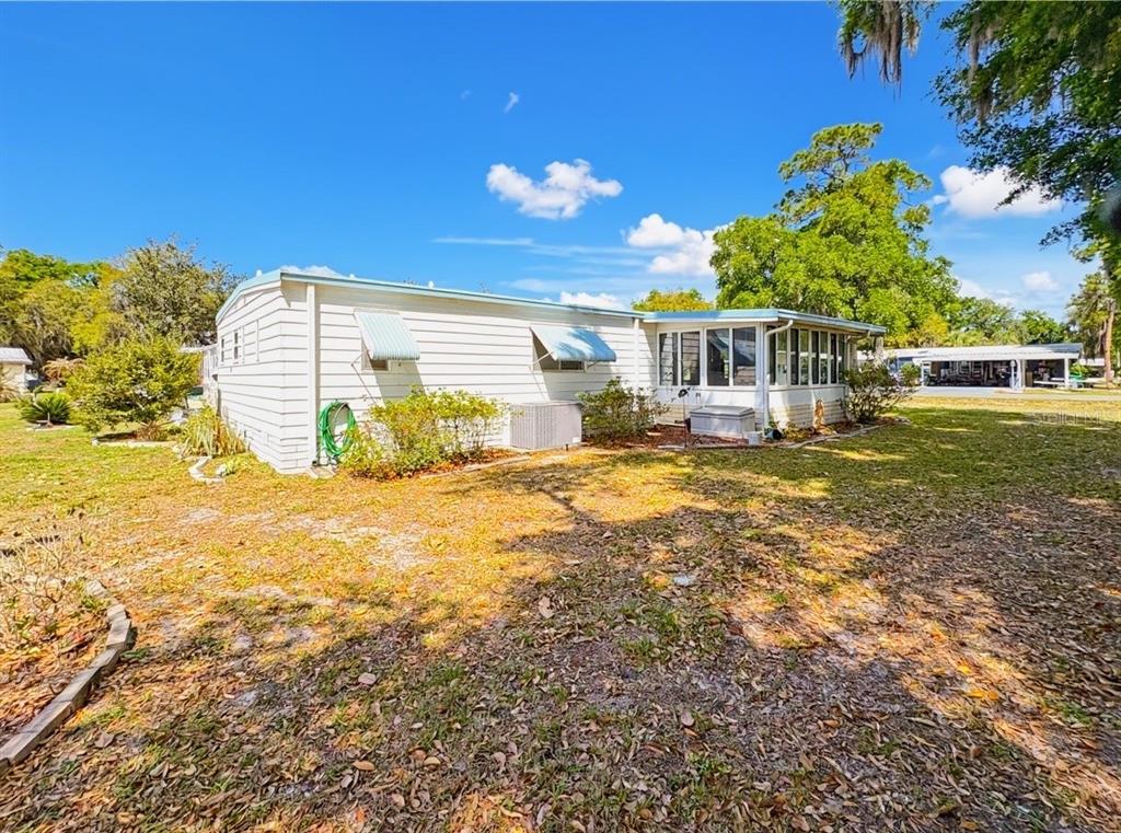 The exterior of a white mobile home features a screened-in porch and a central air unit — 22 S BOBWHITE ROAD, WILDWOOD, FL