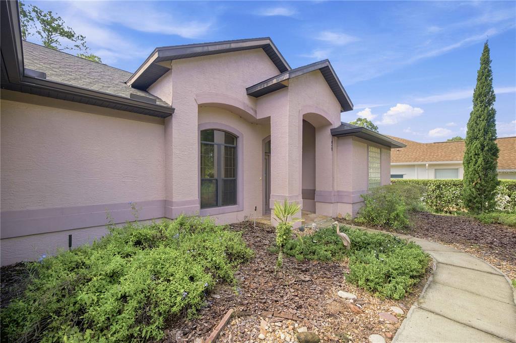 A pink stucco house exterior features a covered entryway, a large window, and landscaped yard — 8939 SW 194TH COURT, DUNNELLON, FL