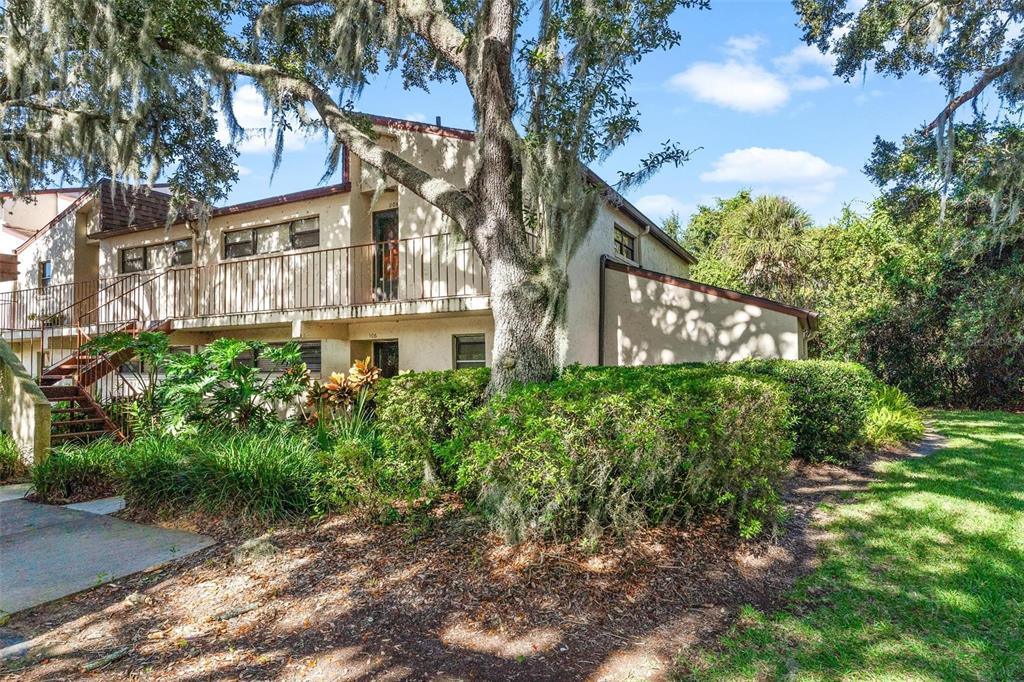 A two-story apartment building with a balcony, exterior stairs, and surrounding trees and bushes — 4300 BAYWOOD BOULEVARD UNIT B106, MOUNT DORA, FL