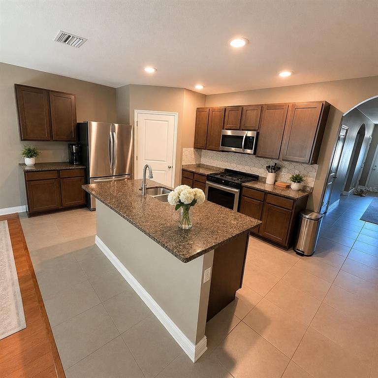 A kitchen features dark wood cabinets, granite countertops, stainless steel appliances, and a central island — 8208 HARWICH PORT LANE, GIBSONTON, FL