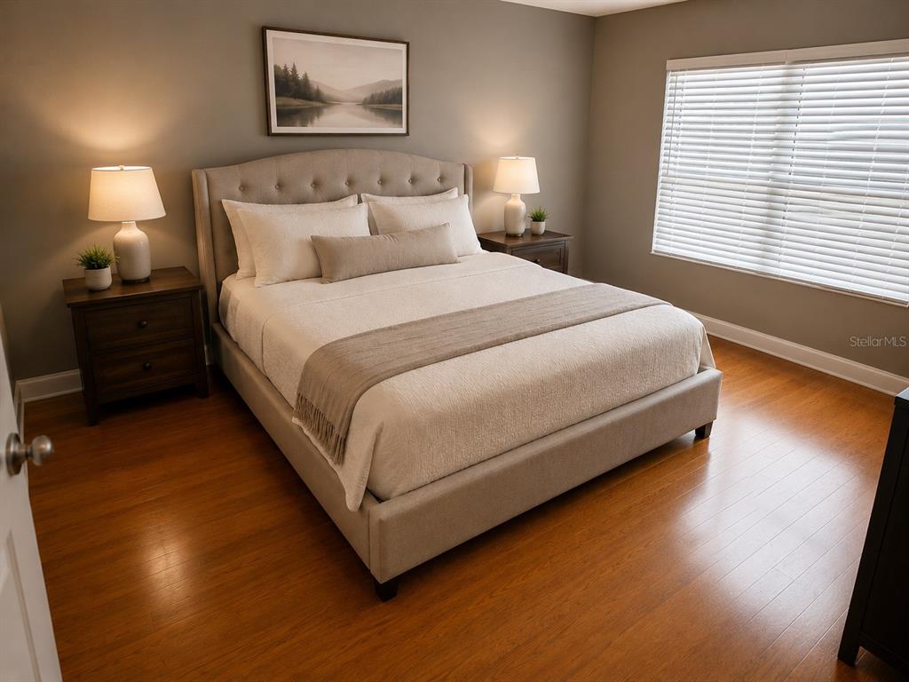 A bedroom features a tufted upholstered bed, wood flooring, two nightstands, and a window with blinds — 8208 HARWICH PORT LANE, GIBSONTON, FL