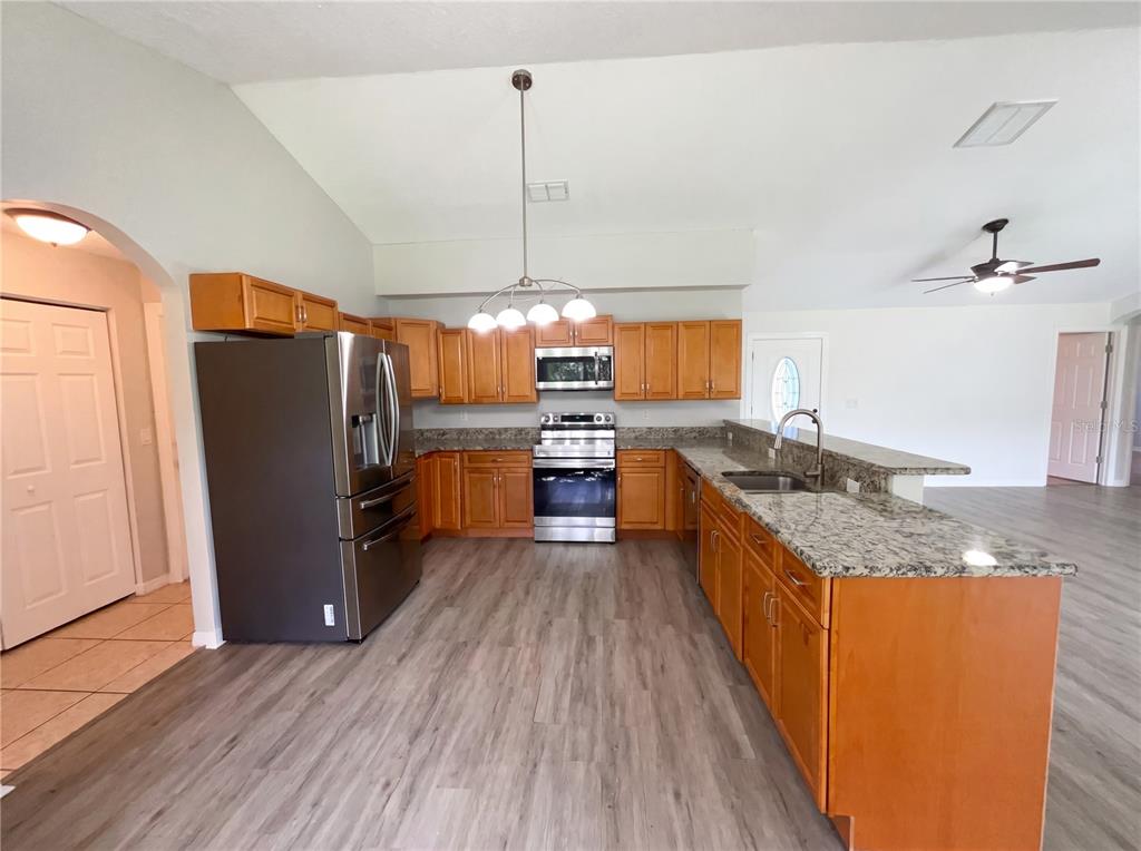 A kitchen features wood cabinets, stainless steel appliances, granite countertops, and light wood-look flooring — 1801 MISSOURI AVENUE, ST CLOUD, FL