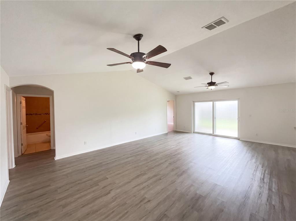A spacious living room features light gray wood-look flooring, vaulted ceilings, and two ceiling fans — 1801 MISSOURI AVENUE, ST CLOUD, FL