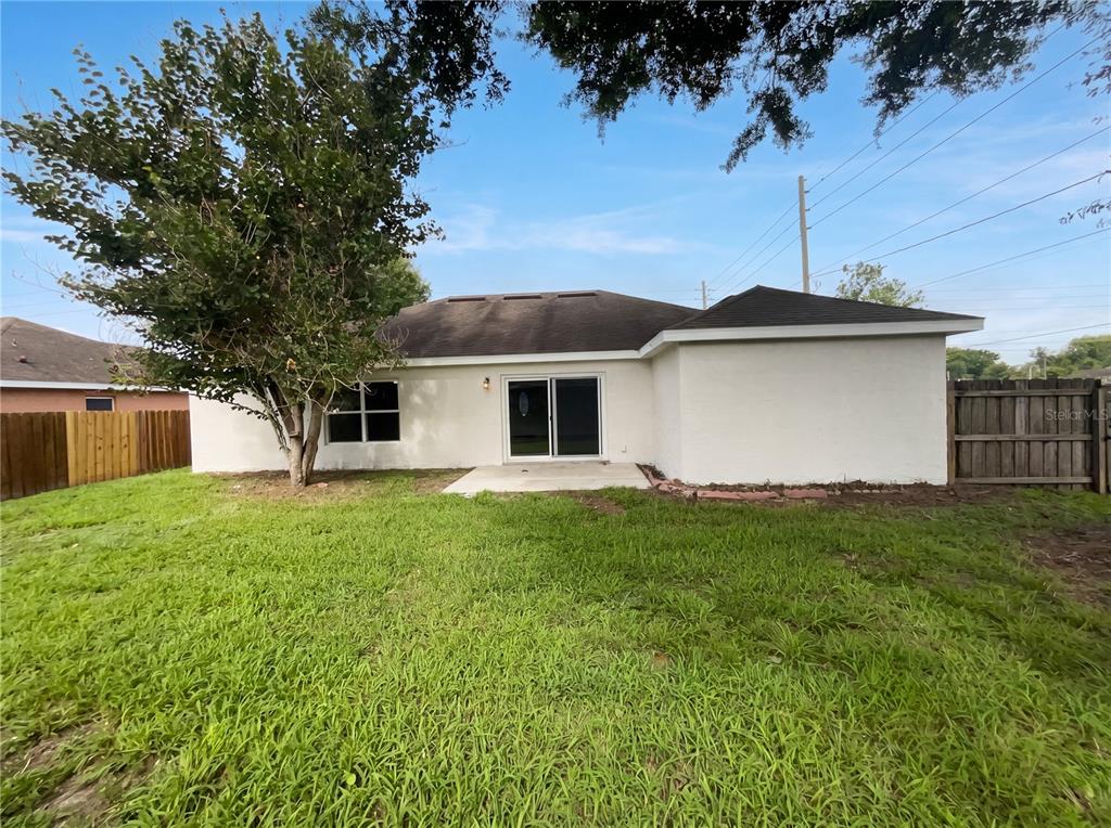 The exterior view of a house shows a backyard with a patio, lawn, and tree — 1801 MISSOURI AVENUE, ST CLOUD, FL