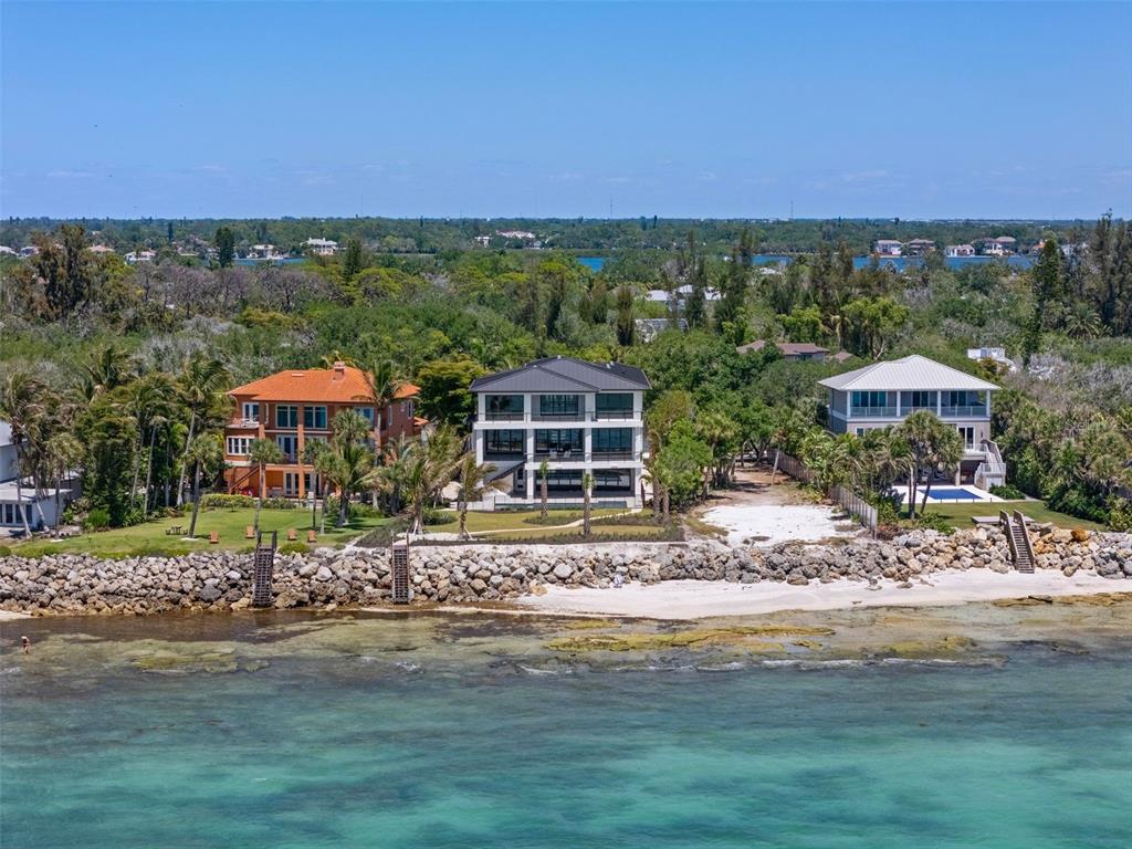 An aerial view shows three large waterfront houses situated along a rocky shoreline and beach — 7324 POINT OF ROCKS ROAD, SARASOTA, FL