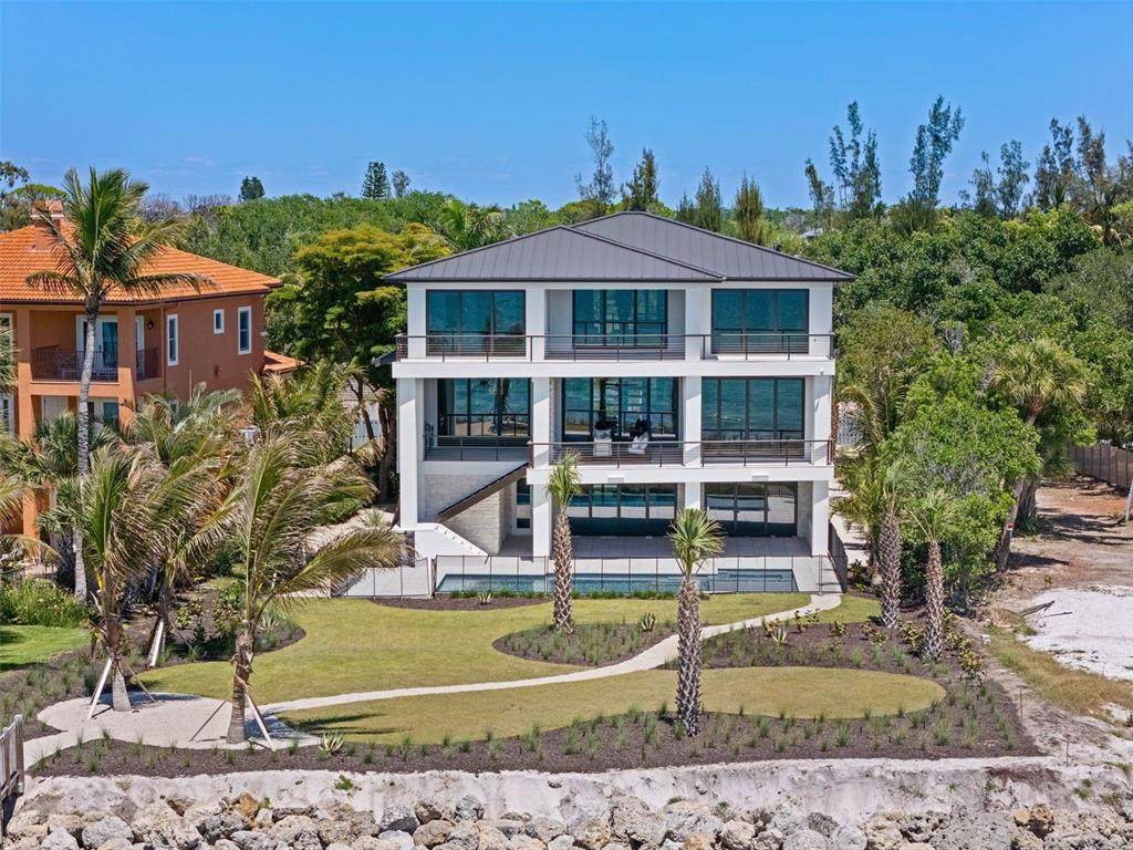 A three-story modern house with balconies and a swimming pool sits near a rocky shoreline — 7324 POINT OF ROCKS ROAD, SARASOTA, FL
