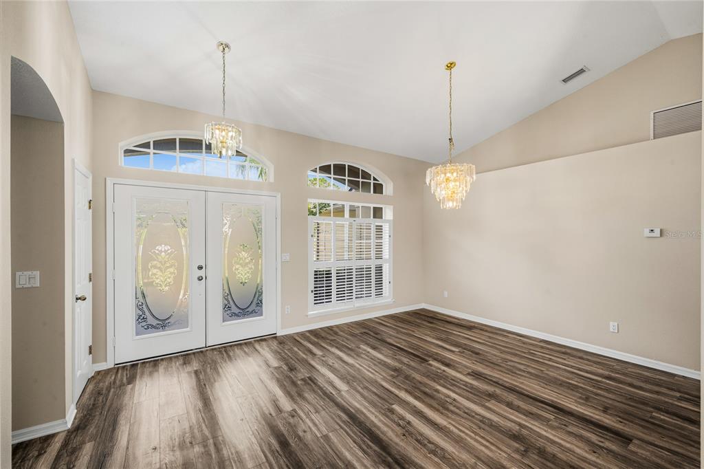 An empty room with wood-look flooring, two crystal chandeliers, and a double front door — 99 HOLLOW PINE DRIVE, DEBARY, FL