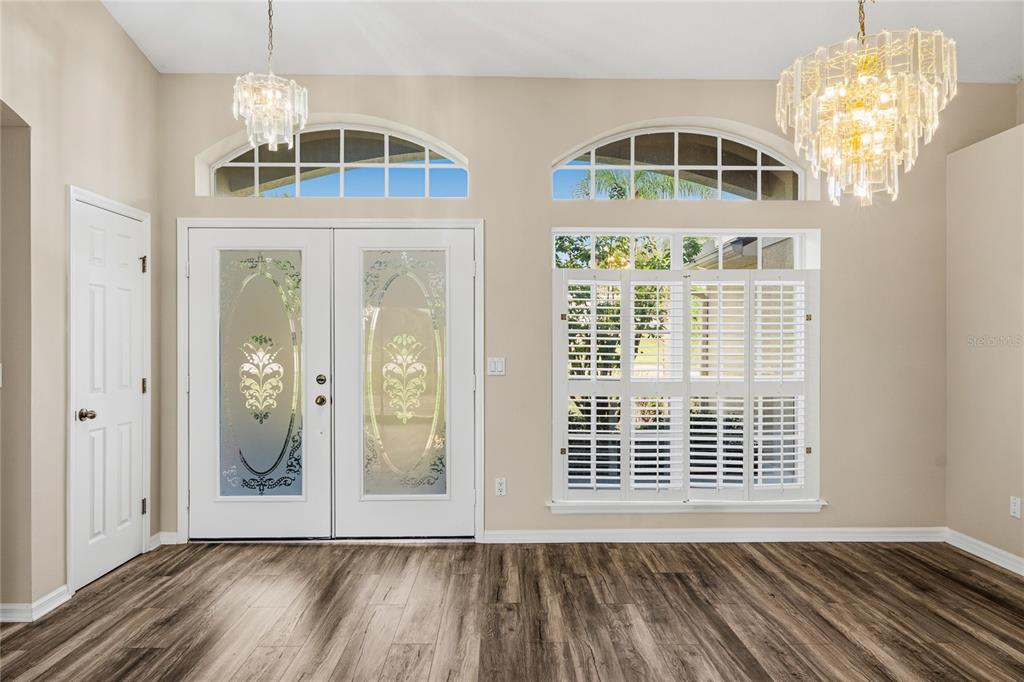 An entryway with wood-look flooring, double glass-paneled doors, arched windows, and two crystal chandeliers — 99 HOLLOW PINE DRIVE, DEBARY, FL