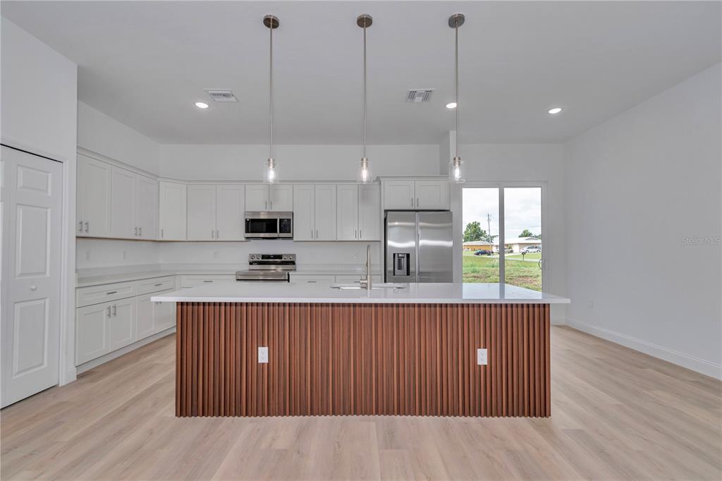 A modern kitchen features white cabinetry, stainless steel appliances, and a slatted wood kitchen island — 13530 SW 47TH CIRCLE, OCALA, FL