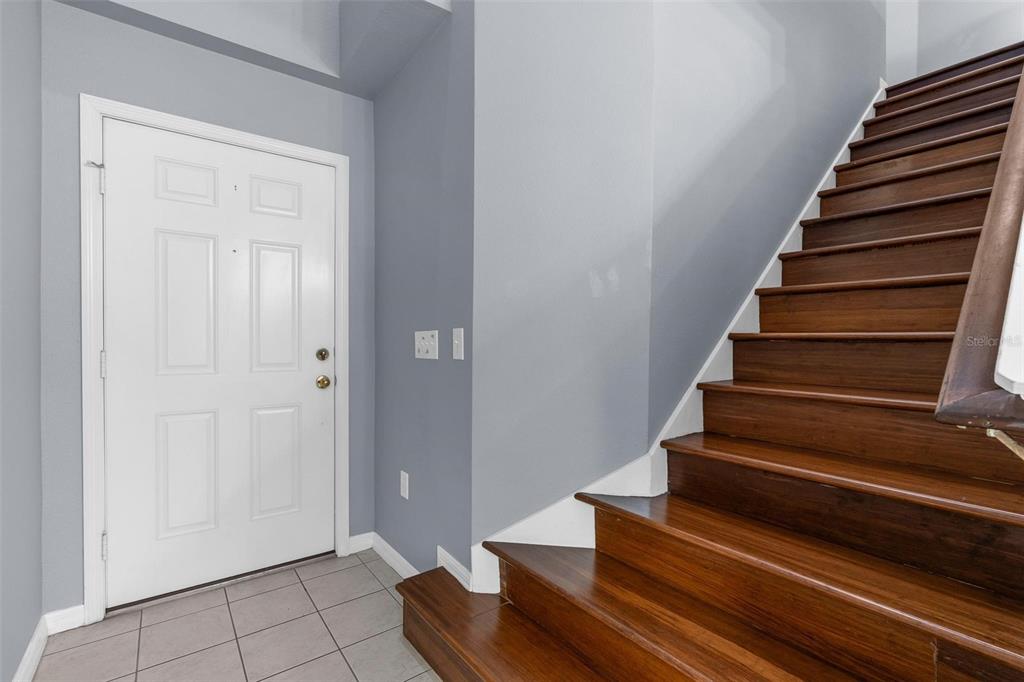 An entryway features a white front door, gray walls, tiled floor, and wooden stairs — 1944 PORTCASTLE CIRCLE, WINTER GARDEN, FL