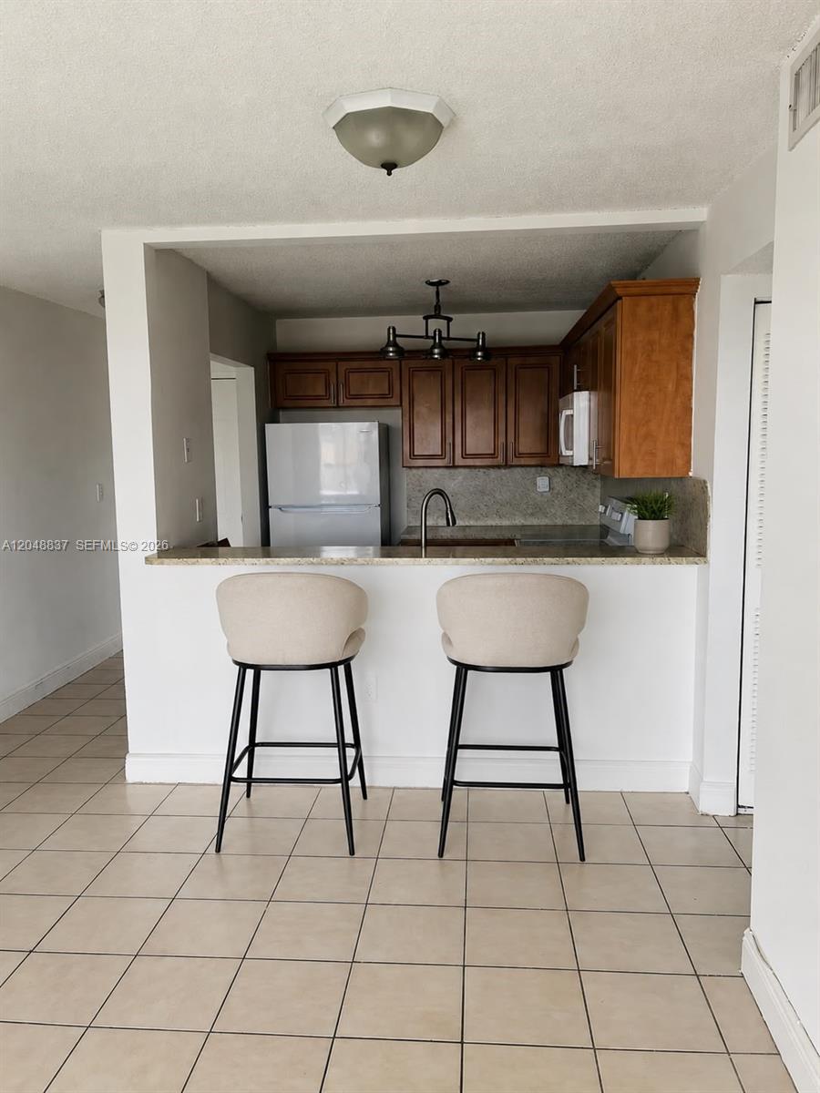 A kitchen with wooden cabinets and a breakfast bar featuring two stools — 8075 NW 7th St # 520, Miami FL 33126, MIAMI, FL