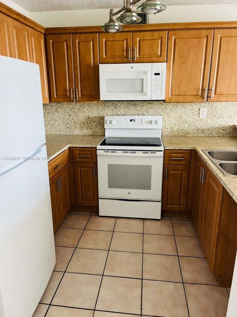 A kitchen features wood cabinets, granite countertops, white appliances, and tiled flooring — 8075 NW 7th St # 520, Miami FL 33126, MIAMI, FL