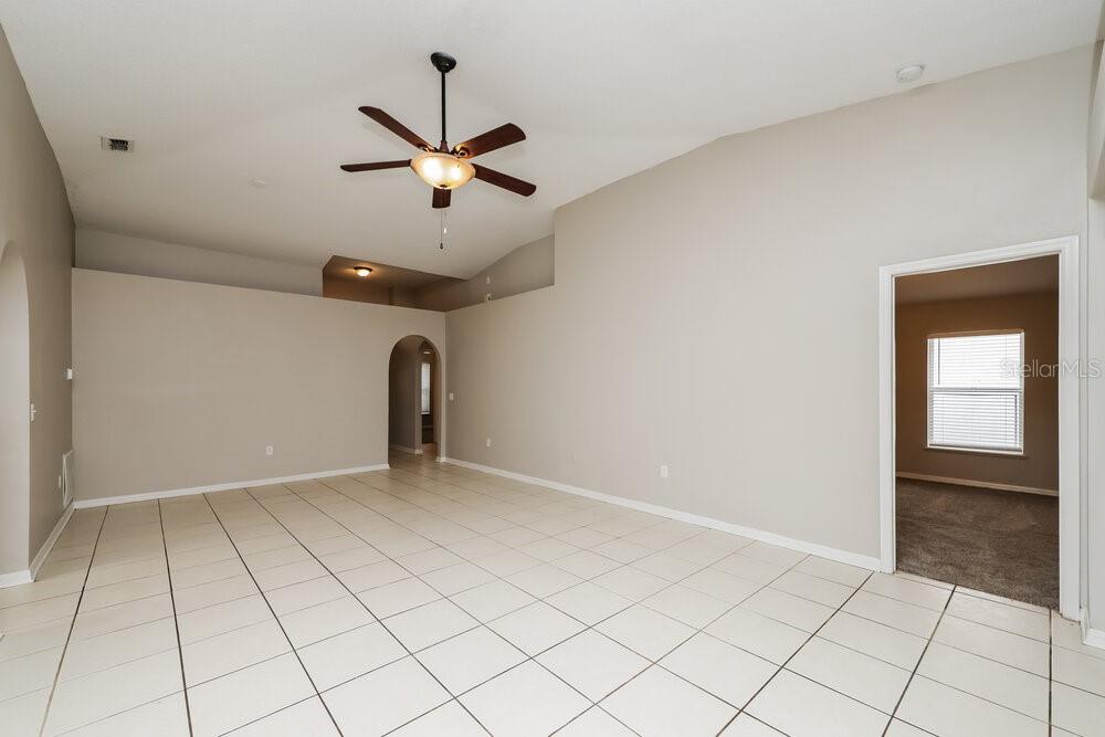 An empty living room features light-colored tile flooring, beige walls, and a vaulted ceiling — 12814 LAKE VISTA DRIVE, GIBSONTON, FL