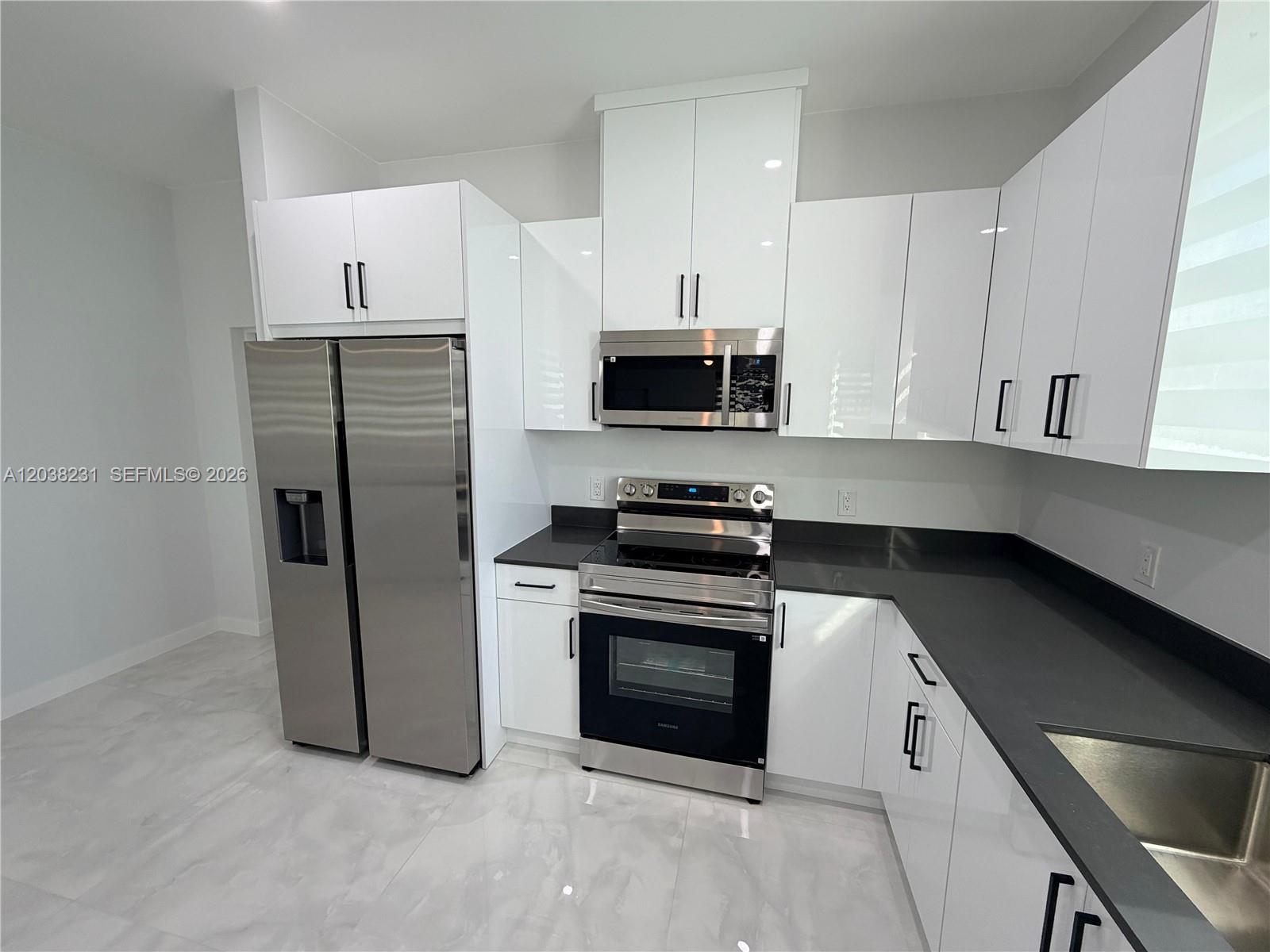 A modern kitchen features white glossy cabinets, stainless steel appliances, and dark gray countertops — 1111 GUNBY AVE S # 1111, Lehigh Acres FL 33974, LEHIGH ACRES, FL