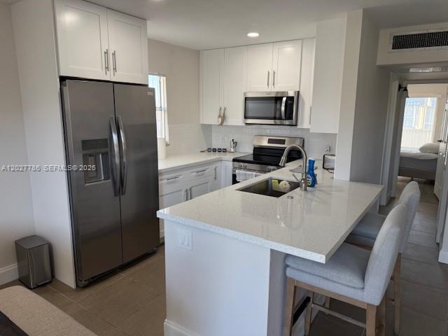 A modern kitchen features white cabinetry, stainless steel appliances, and a quartz-topped island with seating — 417 Brittany I # 417, Delray Beach FL 33446, DELRAY BEACH, FL