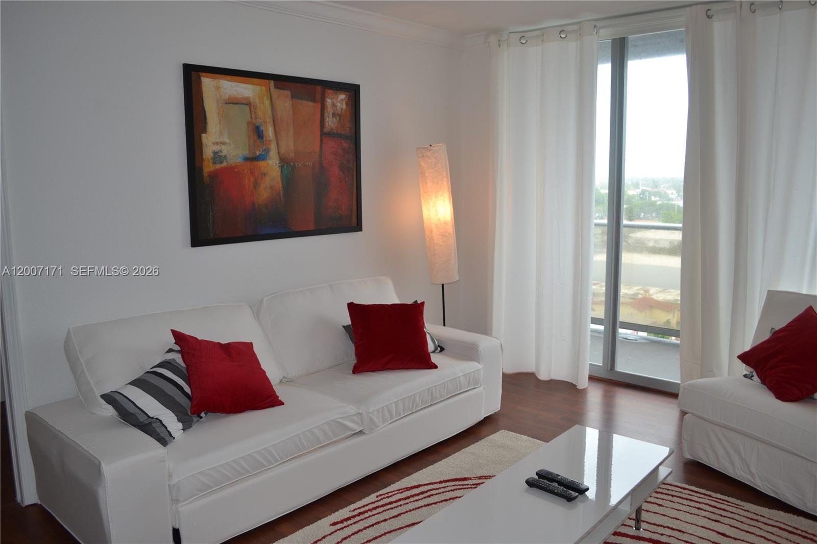 A living room features a white sofa, red accent pillows, a floor lamp, and balcony access — 401 69th St # 1013, Miami Beach FL 33141, MIAMI BEACH, FL