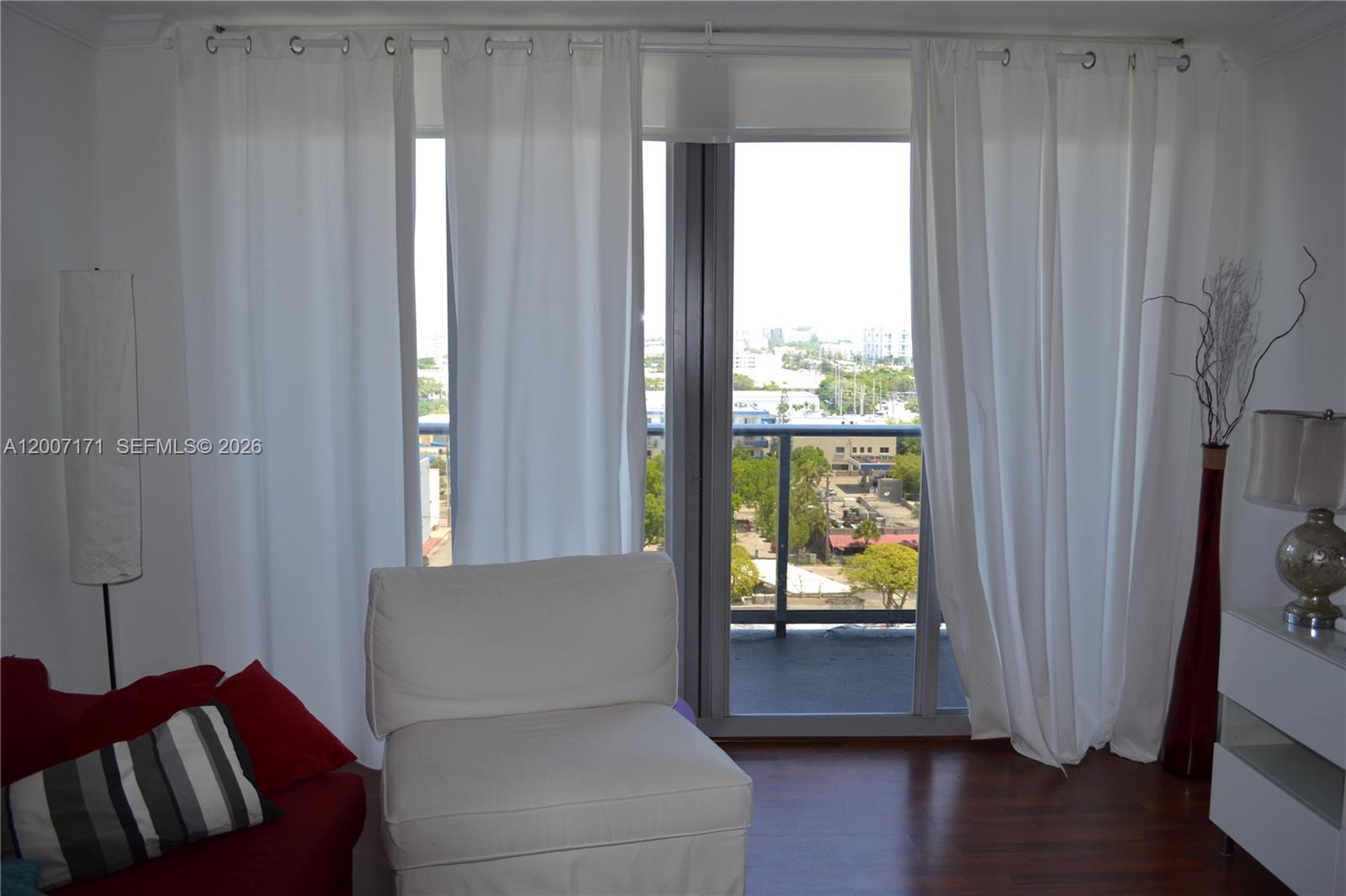 A living room features white curtains, a white chair, and a view of the city — 401 69th St # 1013, Miami Beach FL 33141, MIAMI BEACH, FL