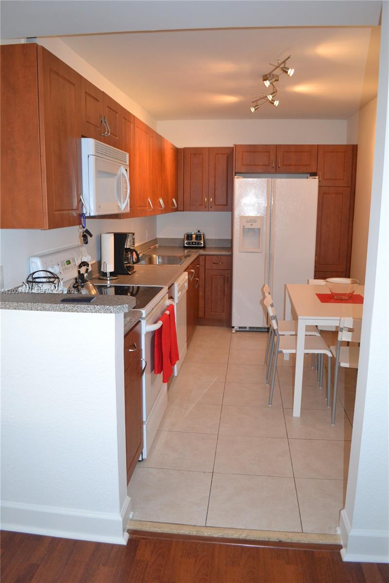 A kitchen features wood cabinets, white appliances, tile flooring, and an adjacent dining area — 401 69th St # 1013, Miami Beach FL 33141, MIAMI BEACH, FL