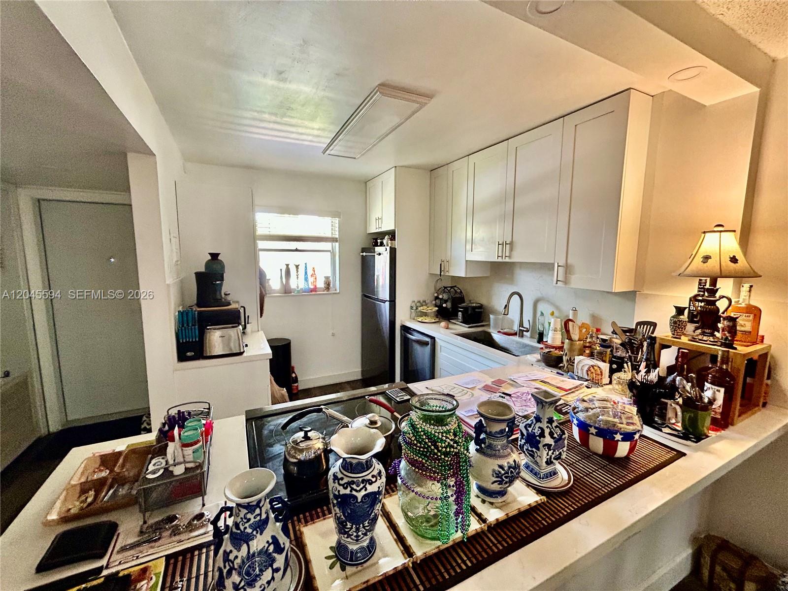 A kitchen features white cabinets, a dark refrigerator, and a counter cluttered with decorative items — 201 Berkley Rd # 104, Hollywood FL 33024, HOLLYWOOD, FL