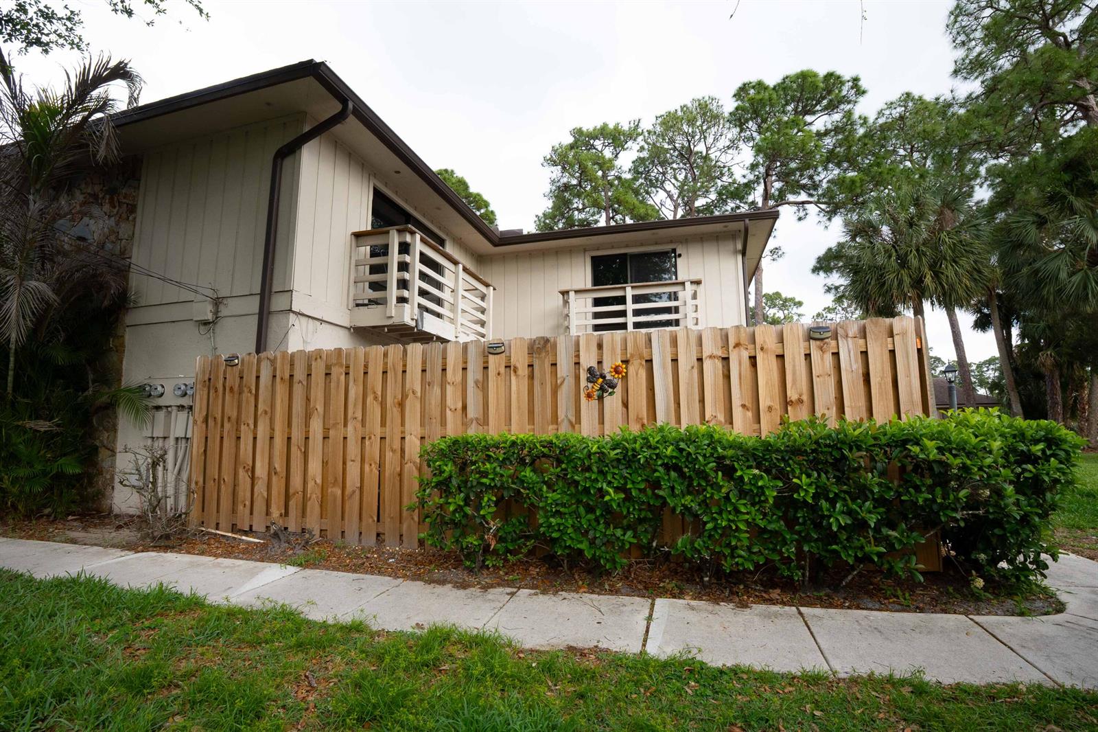 A two-story house with beige siding and wooden balconies sits behind a wooden privacy fence — 2811 Stoneway Lane # B, Fort Pierce FL 34982, FORT PIERCE, FL