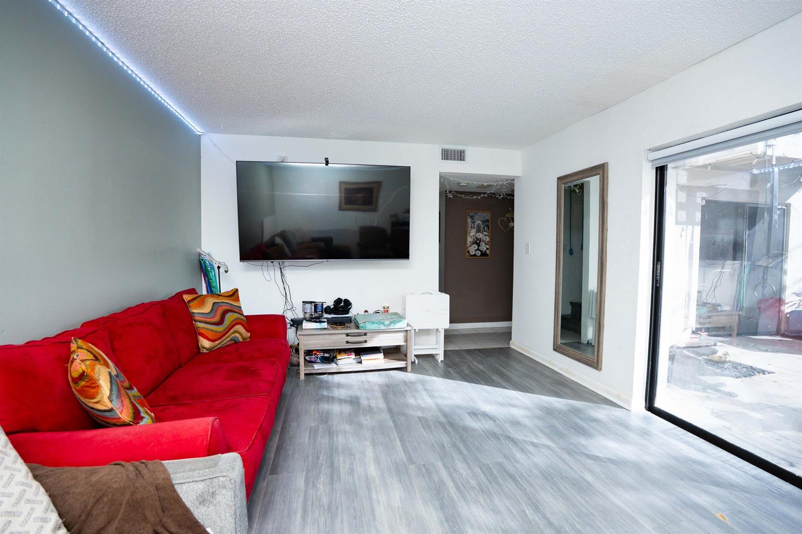 A living room features a red sofa, a wall-mounted television, and sliding glass patio doors — 2811 Stoneway Lane # B, Fort Pierce FL 34982, FORT PIERCE, FL