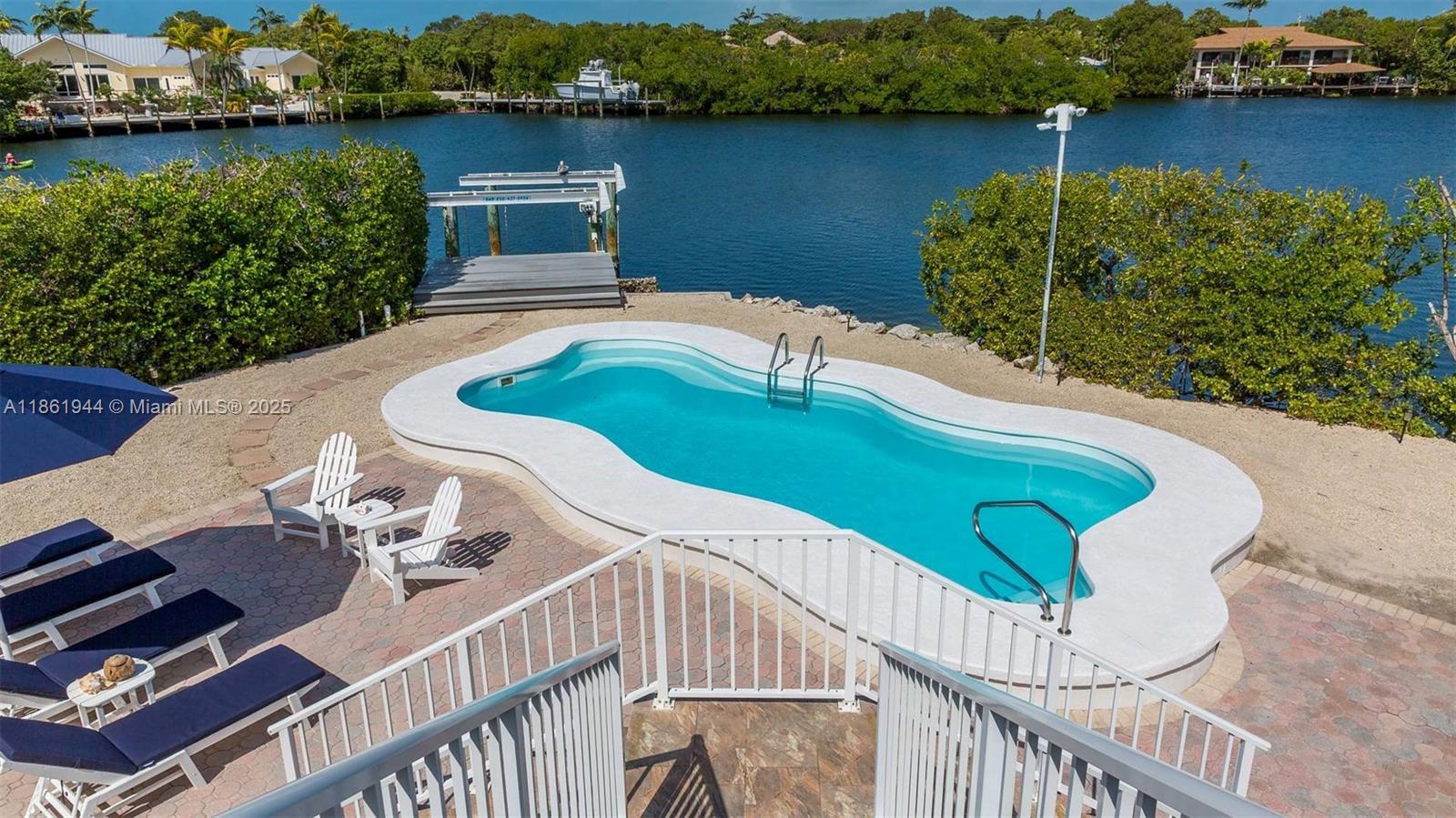 An outdoor swimming pool with a white deck overlooks a canal with a boat dock — 7760 Aviation BLvd. # 0, Marathon FL 33050, MARATHON, FL