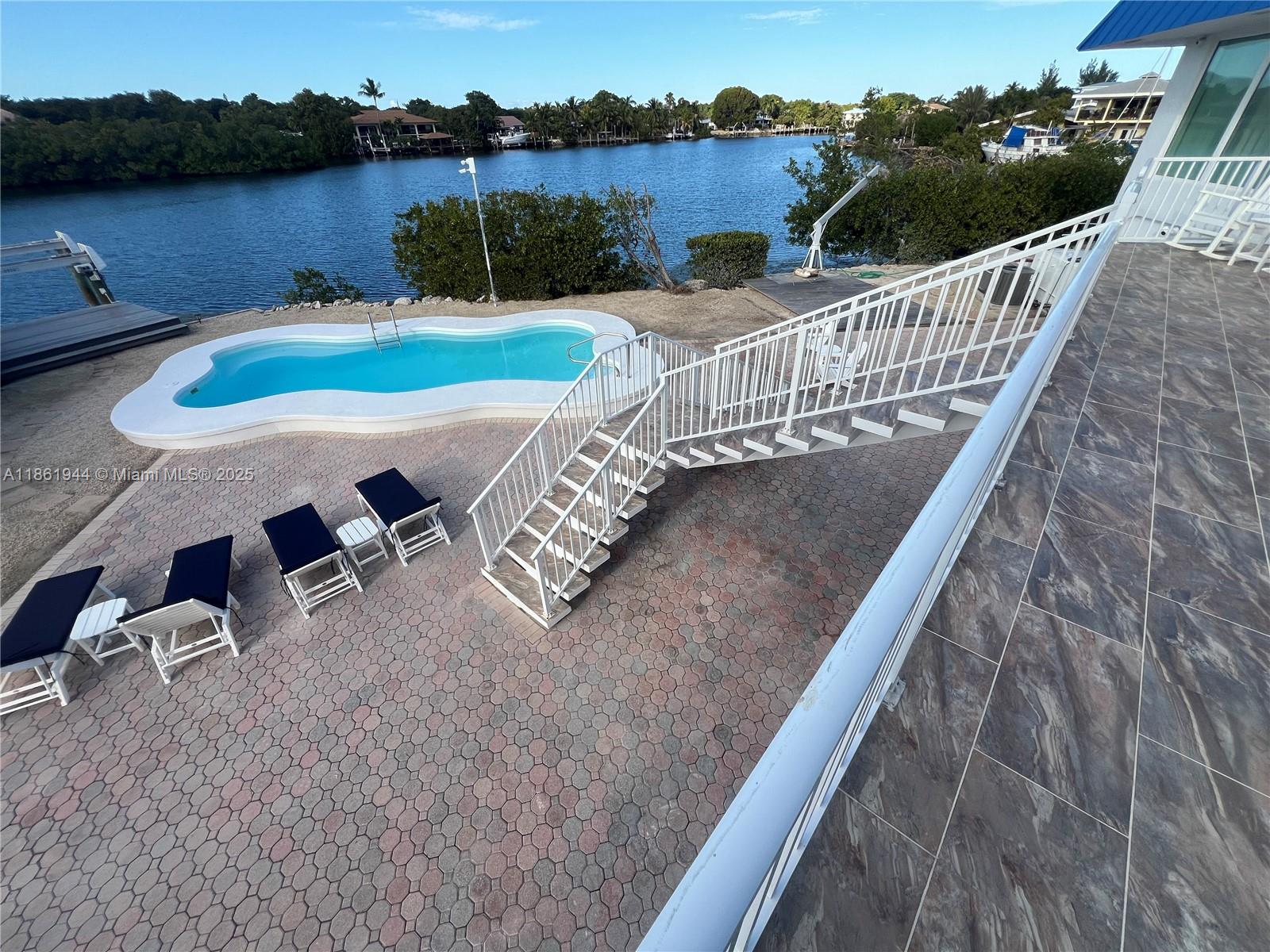 An elevated balcony overlooks a patio with a swimming pool, lounge chairs, and a waterway — 7760 Aviation BLvd. # 0, Marathon FL 33050, MARATHON, FL