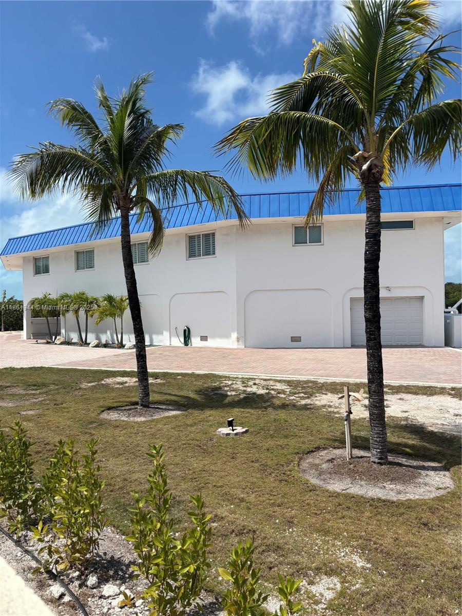 A white two-story house with a blue metal roof stands behind two palm trees — 7760 Aviation BLvd. # 0, Marathon FL 33050, MARATHON, FL