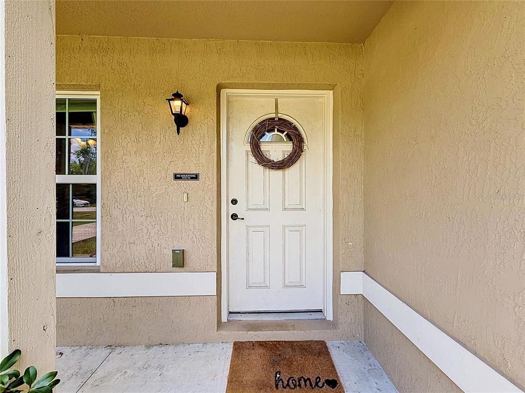 A white front door with a wreath sits on a beige stucco porch — 3 PINE TRACK PLACE, OCALA, FL