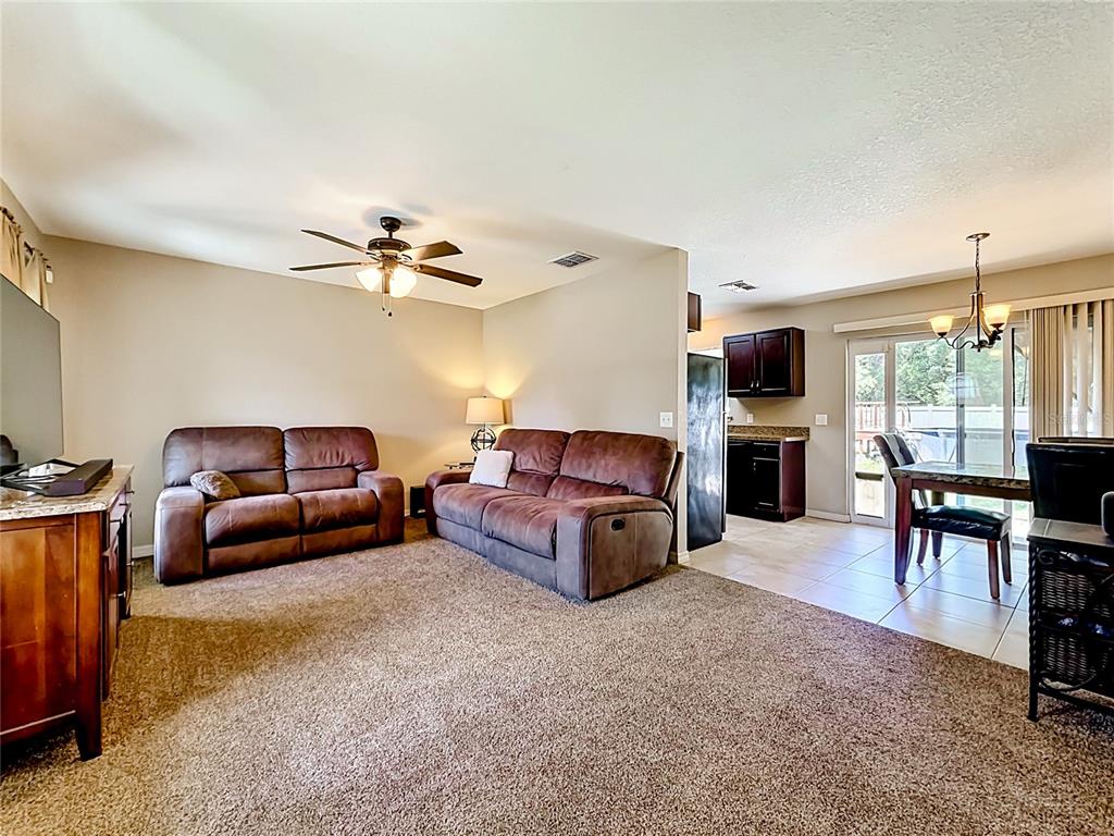 A living room with brown sofas and carpet flows into a kitchen and dining area — 3 PINE TRACK PLACE, OCALA, FL