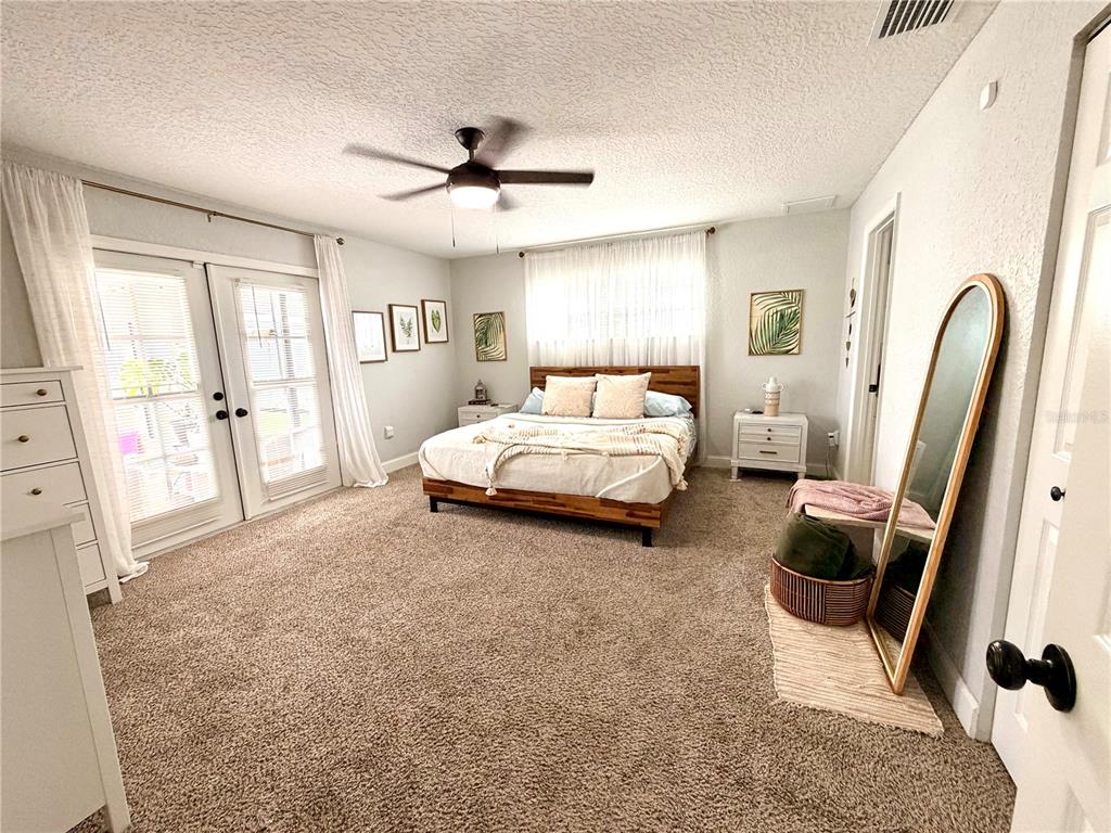 A bedroom features a wooden bed frame, carpeted flooring, French doors, and a full-length mirror — 11450 LINDEN DRIVE, SPRING HILL, FL